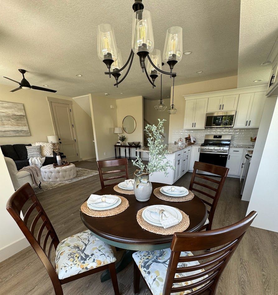Dining area with round table, four chairs, chandelier, and open view to kitchen and living room.