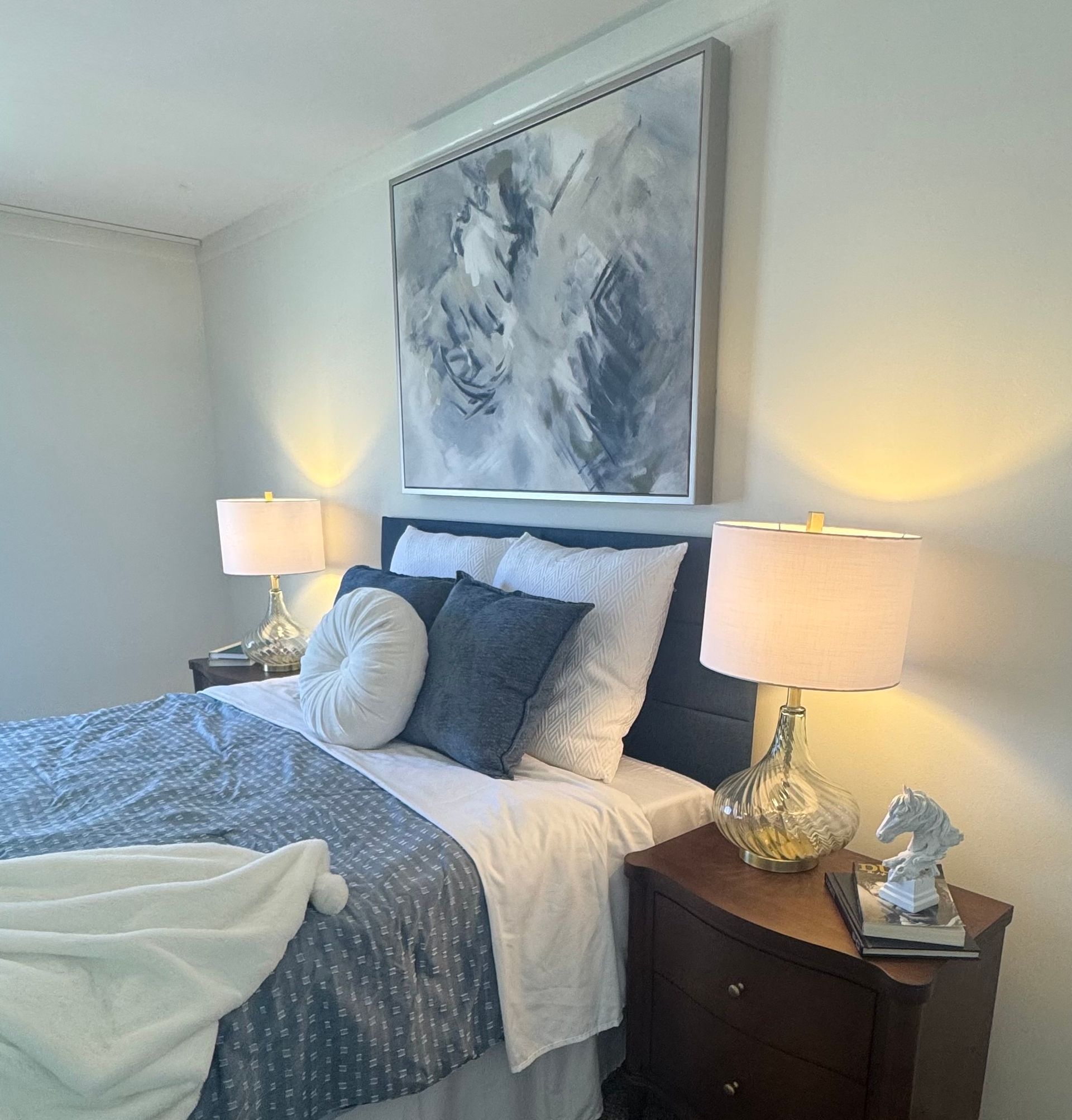 Bedroom with a bed, nightstands, lamps, and artwork. Blue and white color scheme.