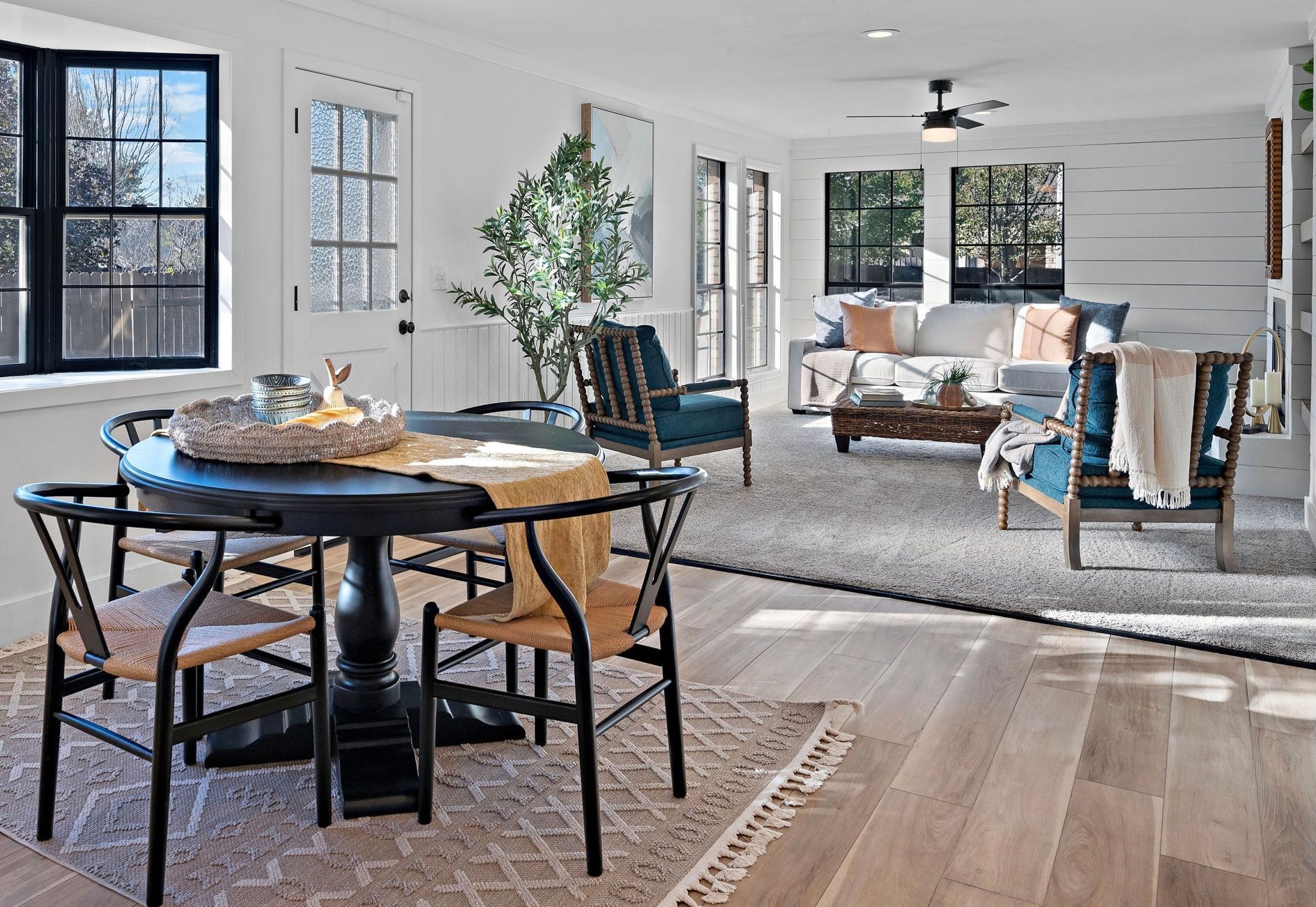Living room with dining table, chairs, sofa, armchairs, hardwood floor, natural light.