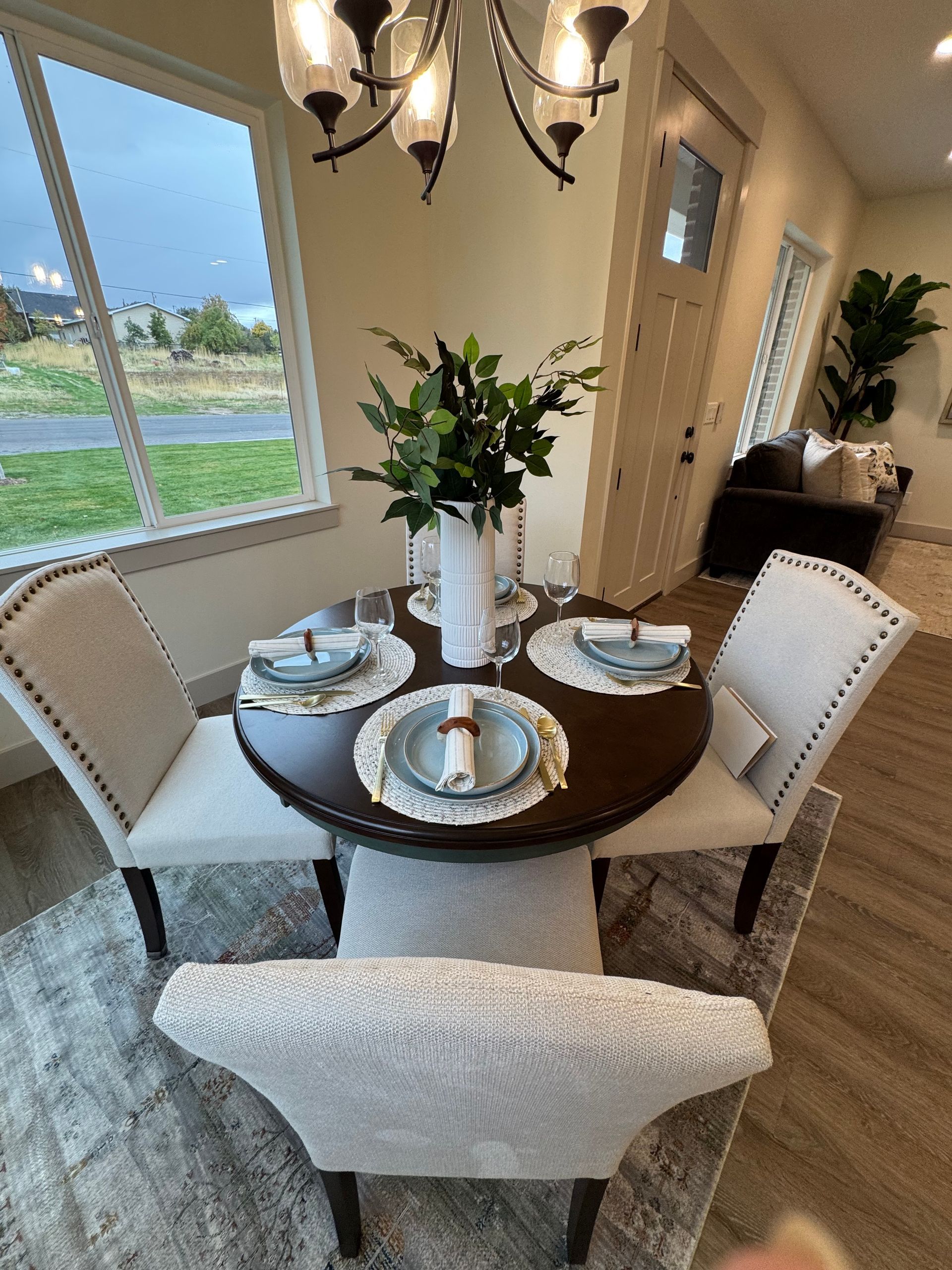 Round dining table set for four, with centerpiece and chandelier in a bright interior.
