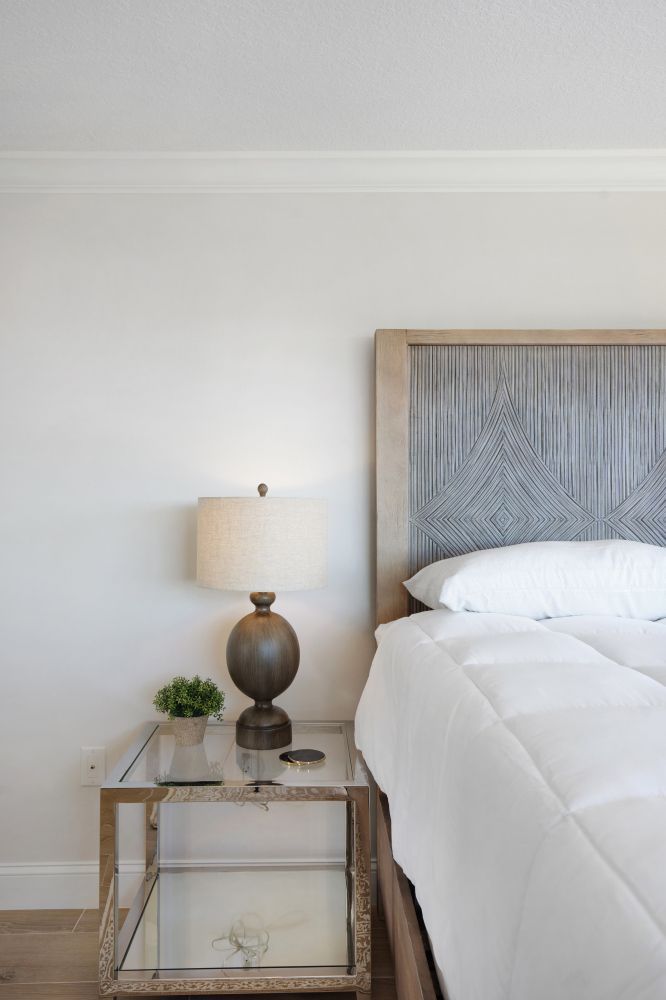 A bedroom with a bed , nightstand , lamp and white sheets.