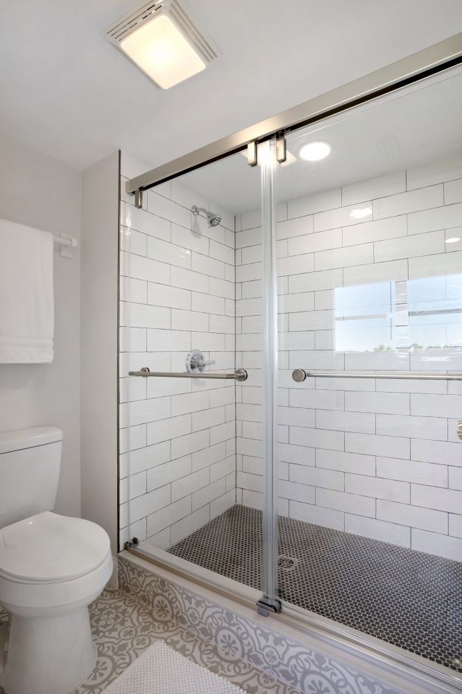 A bathroom with white tiles , a toilet , and a walk in shower.