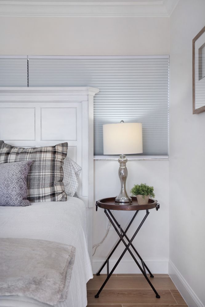 A bedroom with a bed , nightstand , lamp and window.