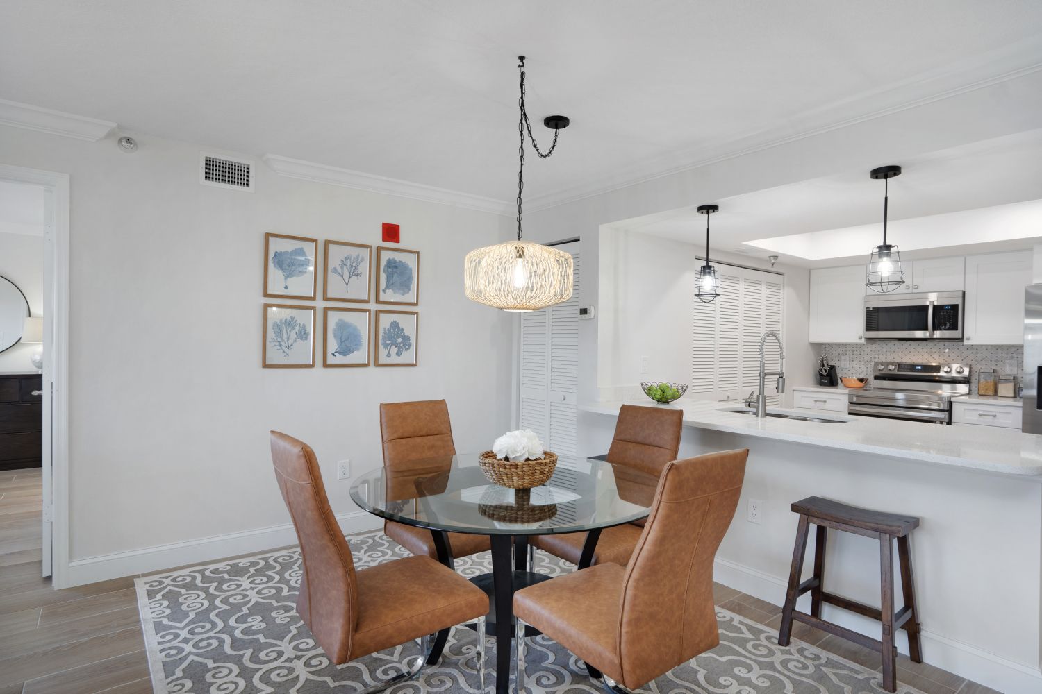 A dining room with a table and chairs and a kitchen in the background.