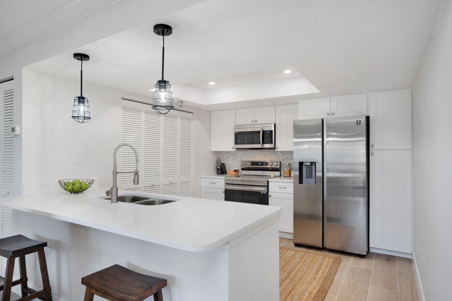A kitchen with white cabinets , stainless steel appliances , a refrigerator and a sink.
