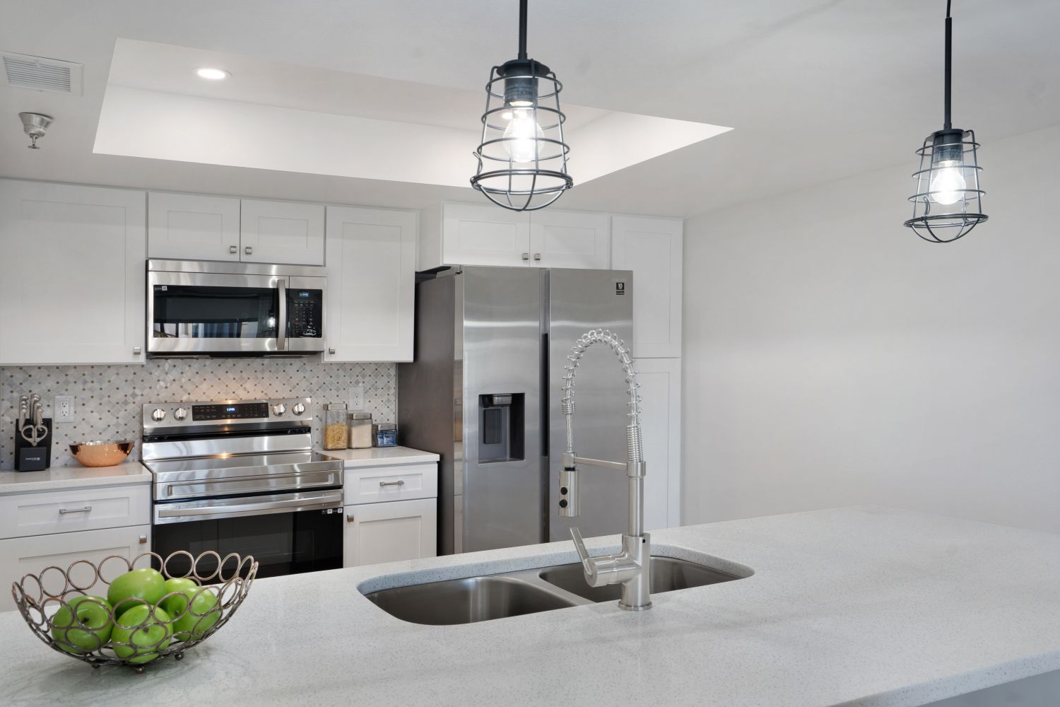 A kitchen with stainless steel appliances and a bowl of apples on the counter.