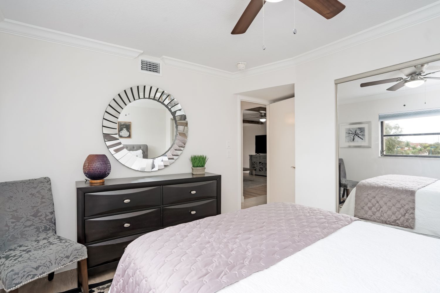 A bedroom with a bed , dresser , chair , mirror and ceiling fan.