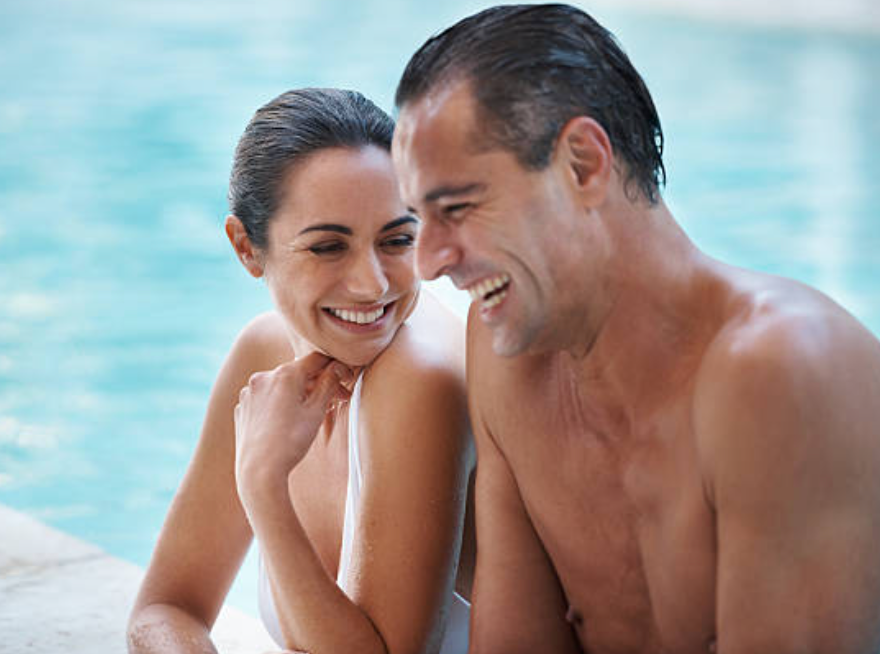 A man and a woman are sitting next to a swimming pool.