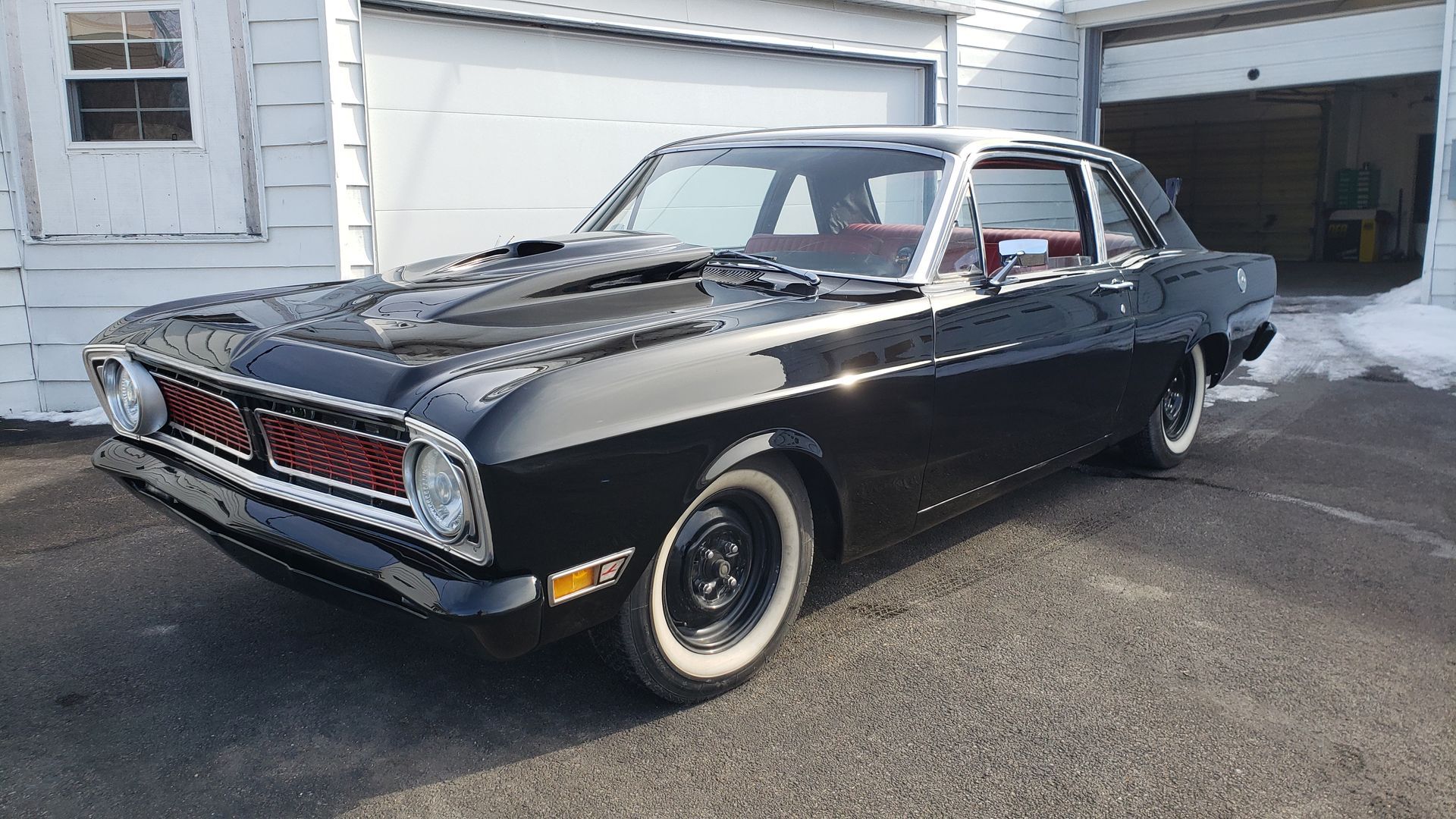 Black vintage car with white-wall tires parked on a driveway in front of a garage.