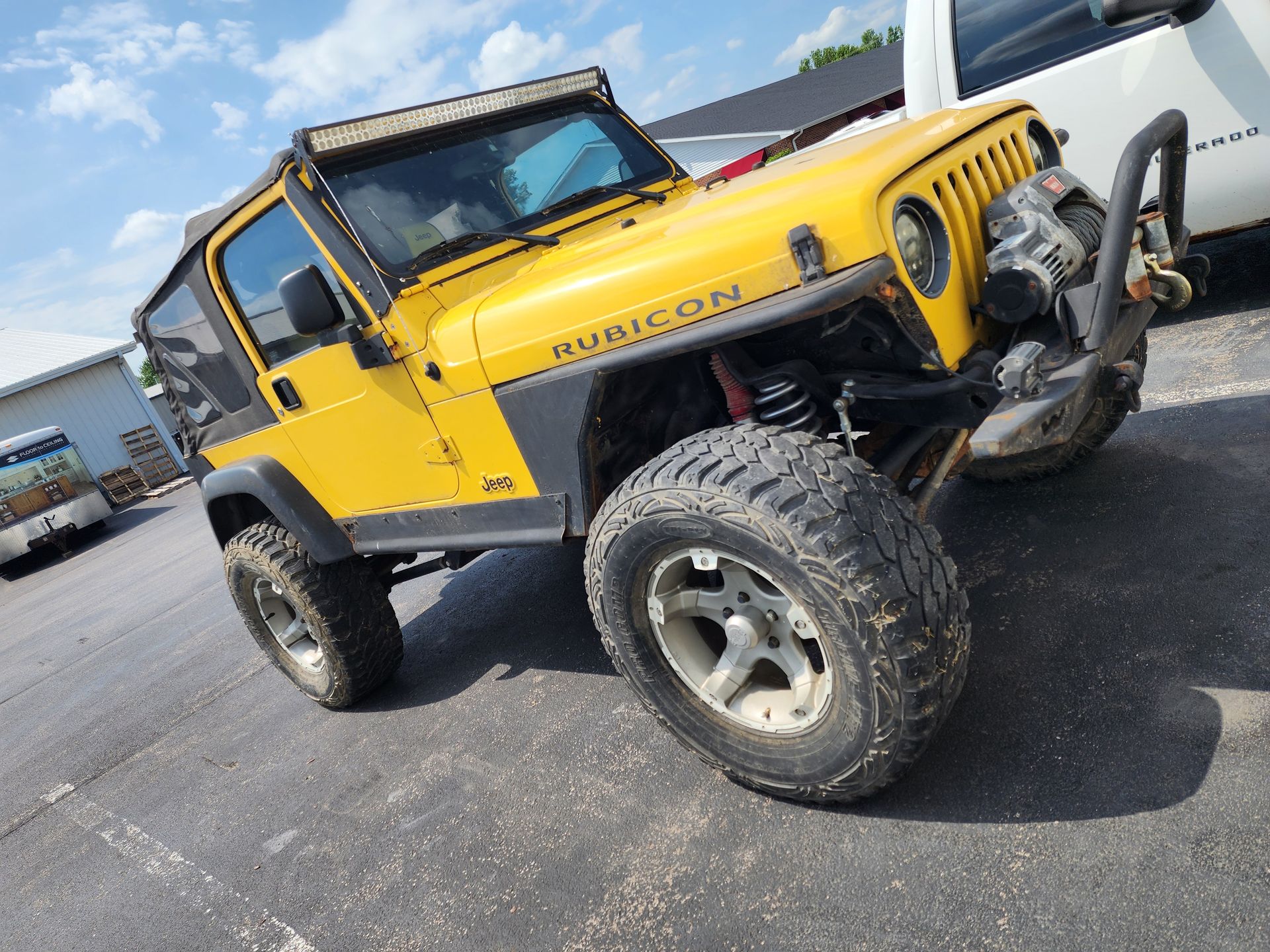 Yellow Jeep Rubicon with large tires, parked on asphalt.