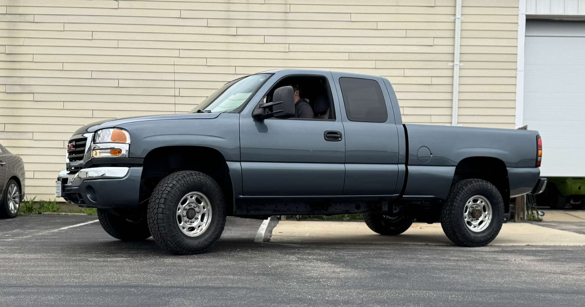 Blue Ford Mustang with white stripes in a garage next to a blue car. Tools and boxes are present.