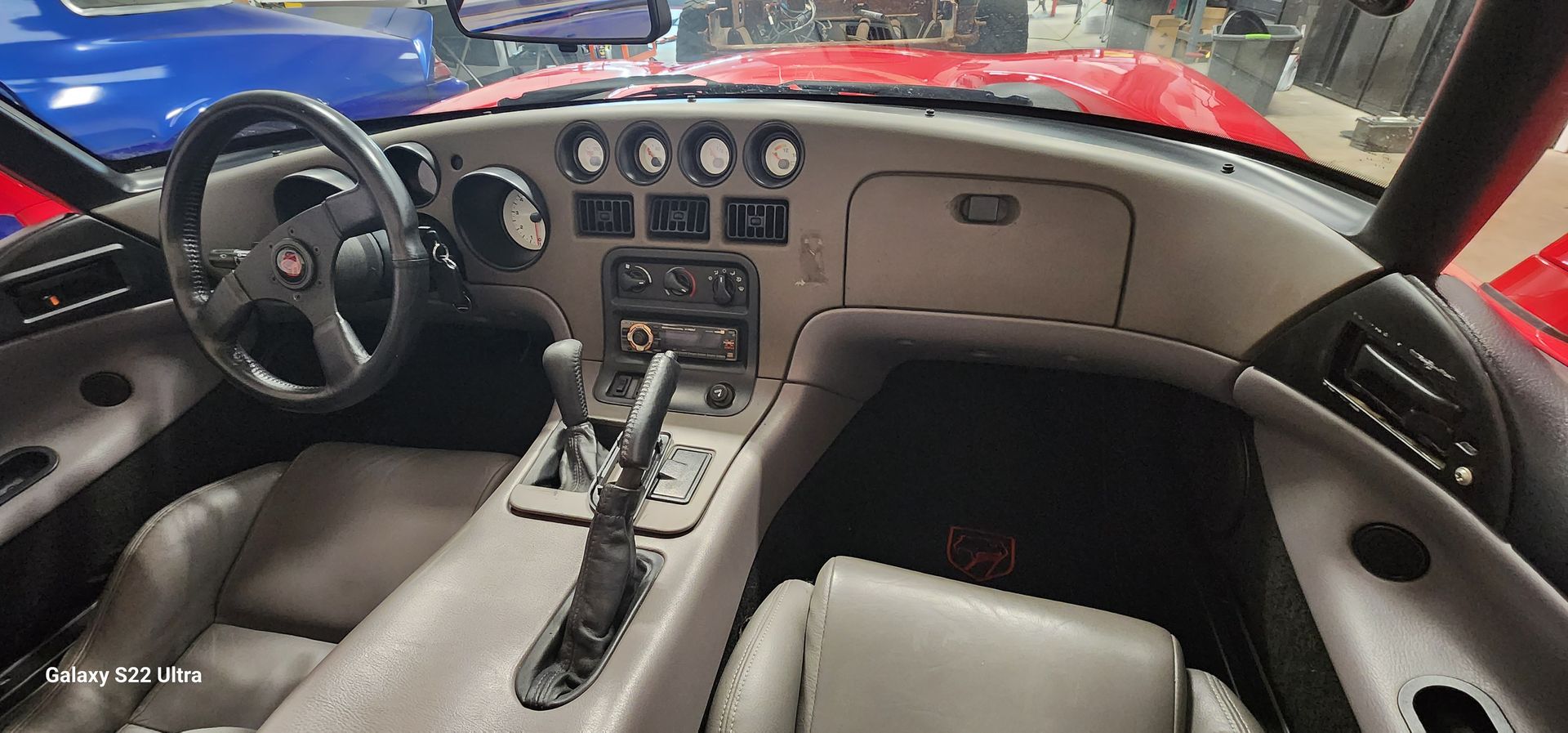 Interior of a red Dodge Viper. Dashboard with gauges, steering wheel, gray seats, and a manual gear shift.