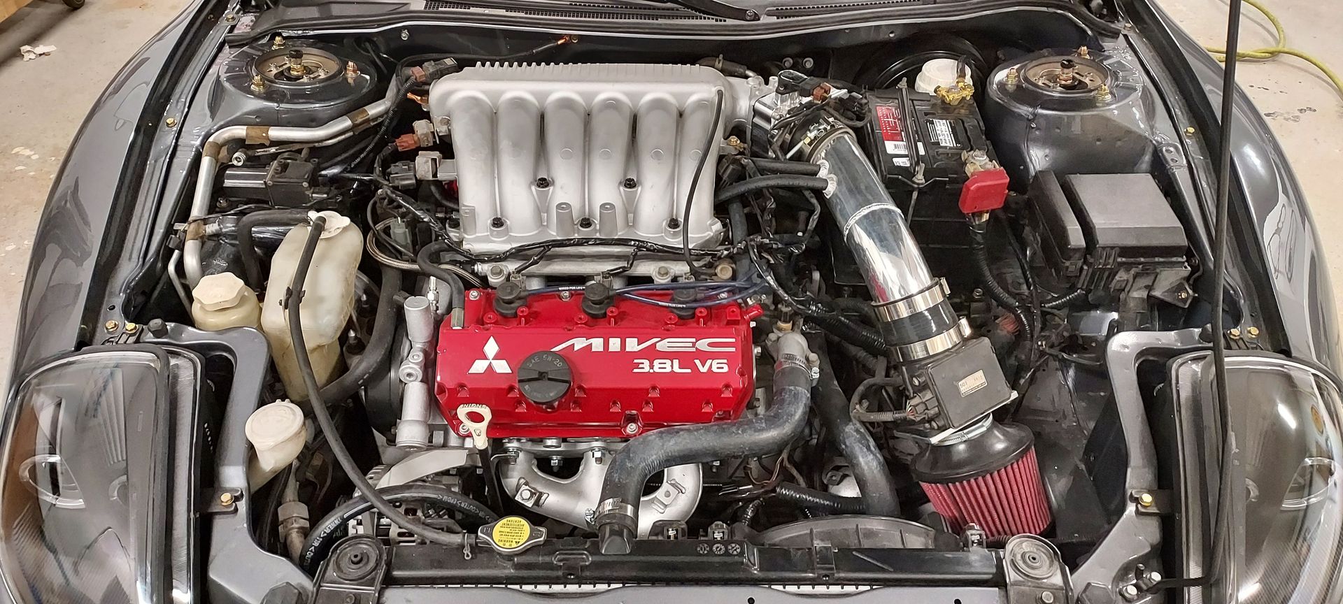 A car engine bay with a red Mitsubishi 3.0L V6 engine, cold air intake, and silver intake manifold.
