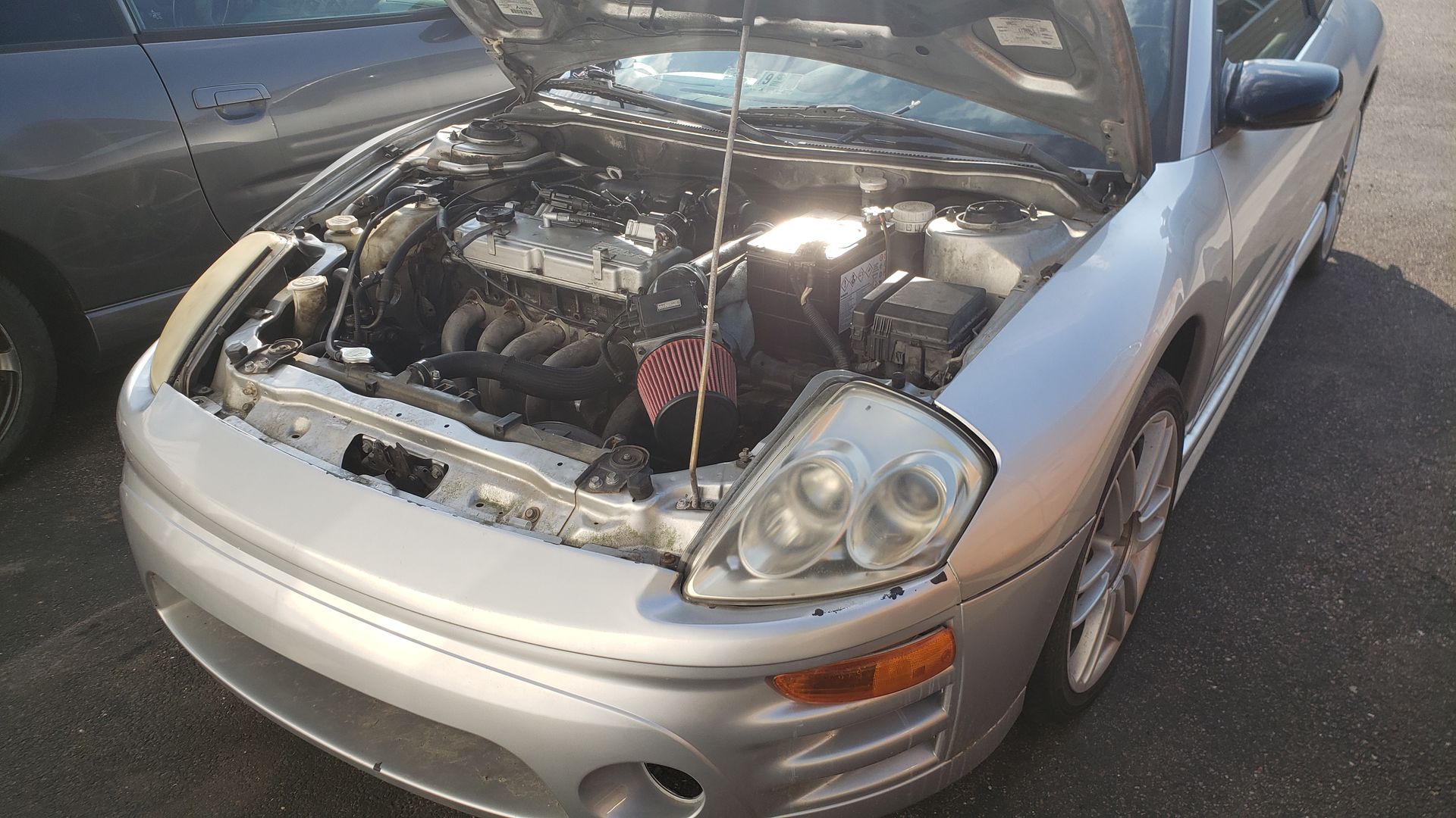 Silver car with open hood, engine visible. Sunlight illuminates the engine bay.