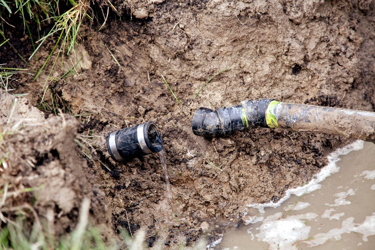 Broken black pipe in muddy ground, water leaking.