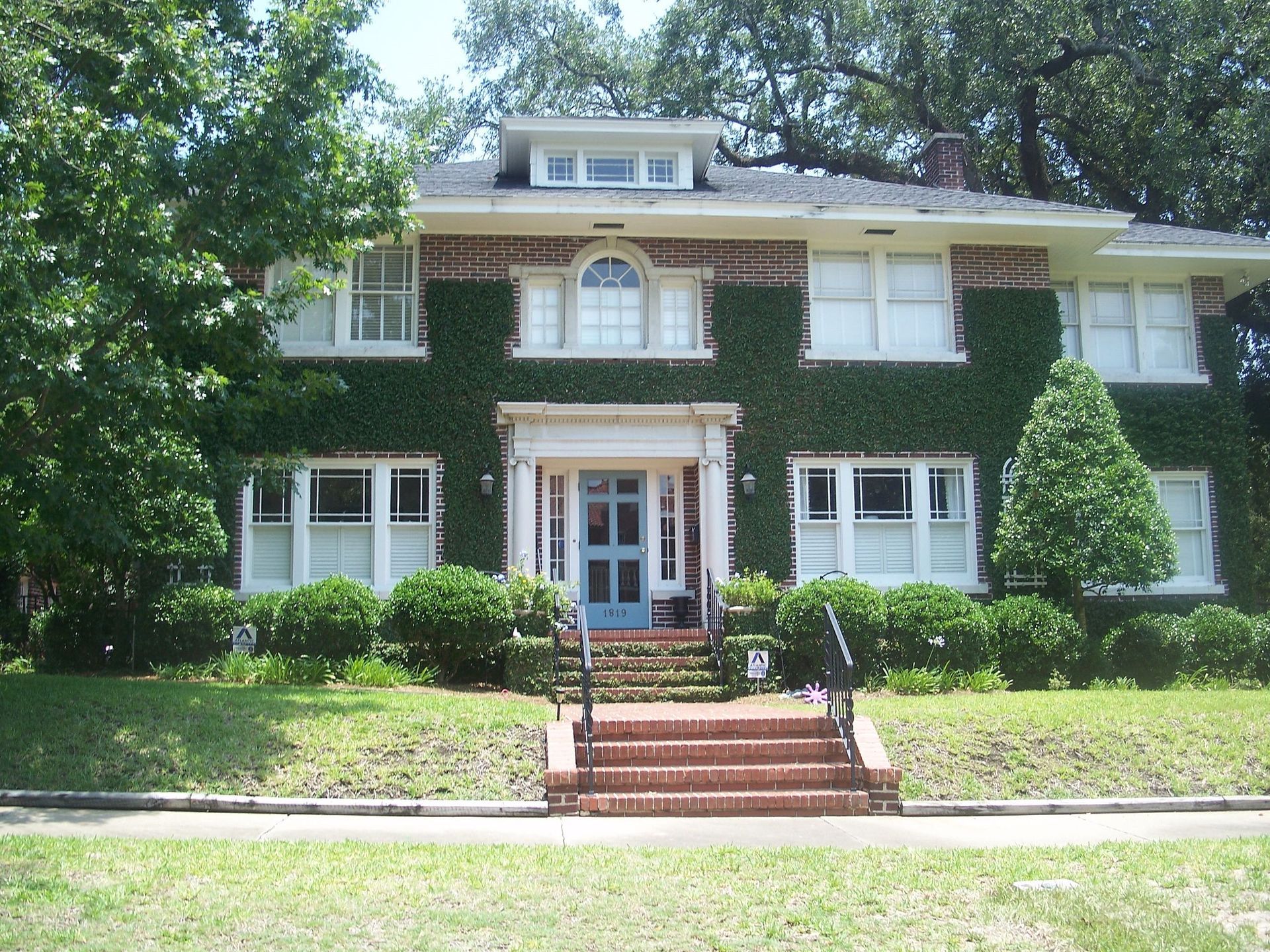 Two-story house with brick steps and a blue door, covered in ivy. White windows, green lawn.