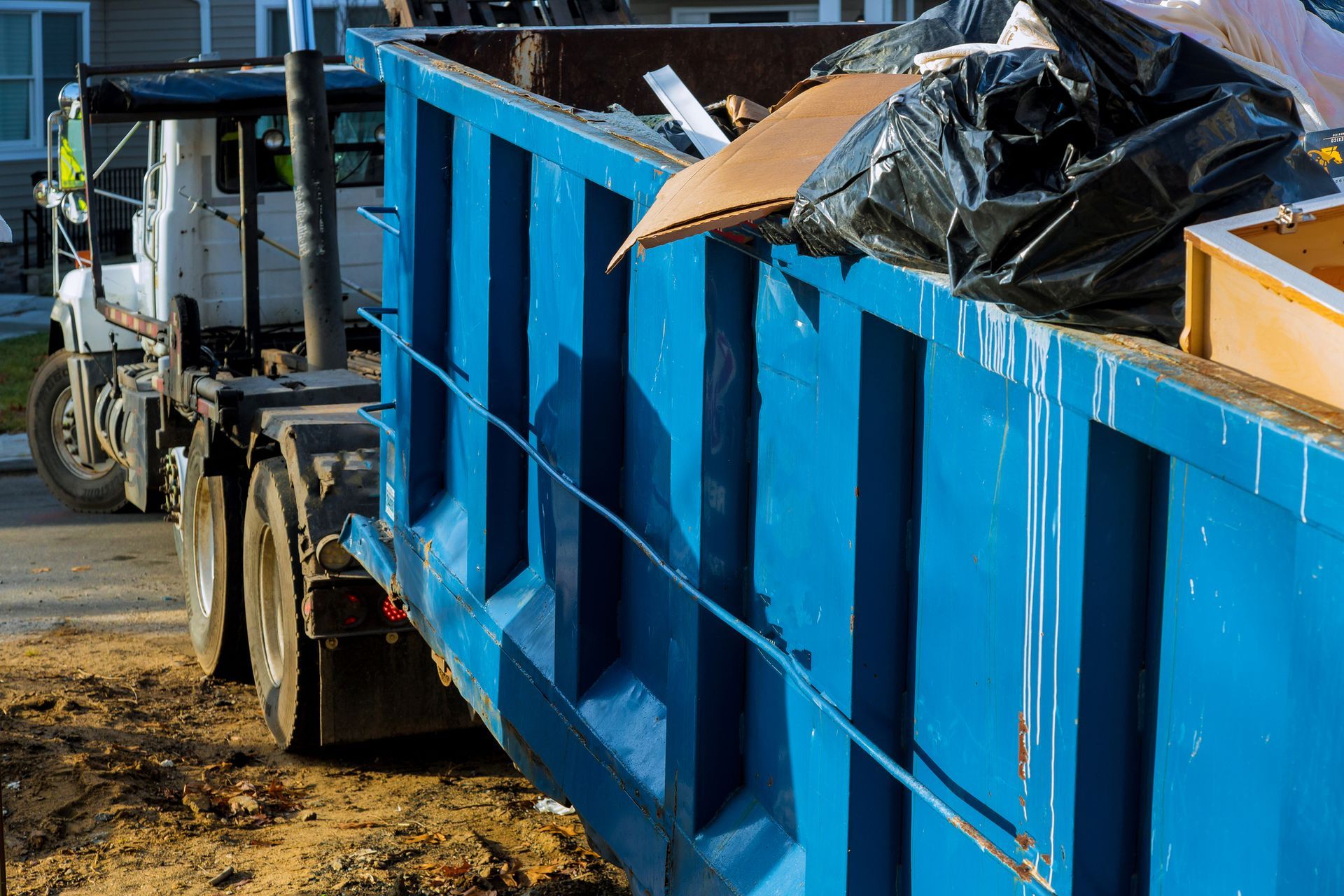 A blue dumpster is sitting on the side of the road next to a truck.