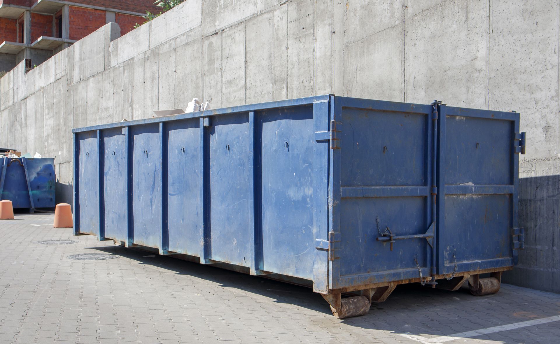 A large blue dumpster is parked in front of a concrete wall.