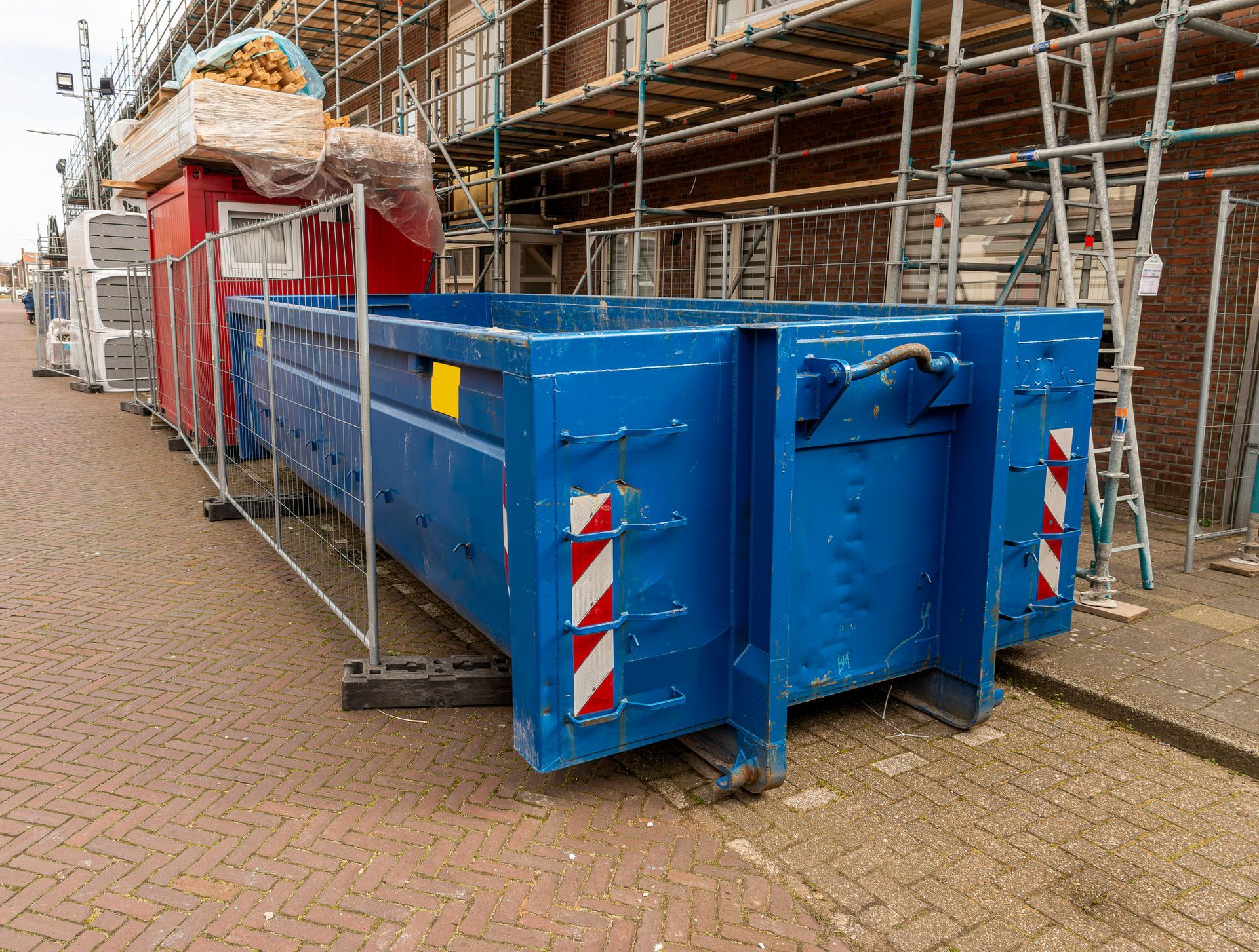 A blue dumpster is parked in front of a building under construction.