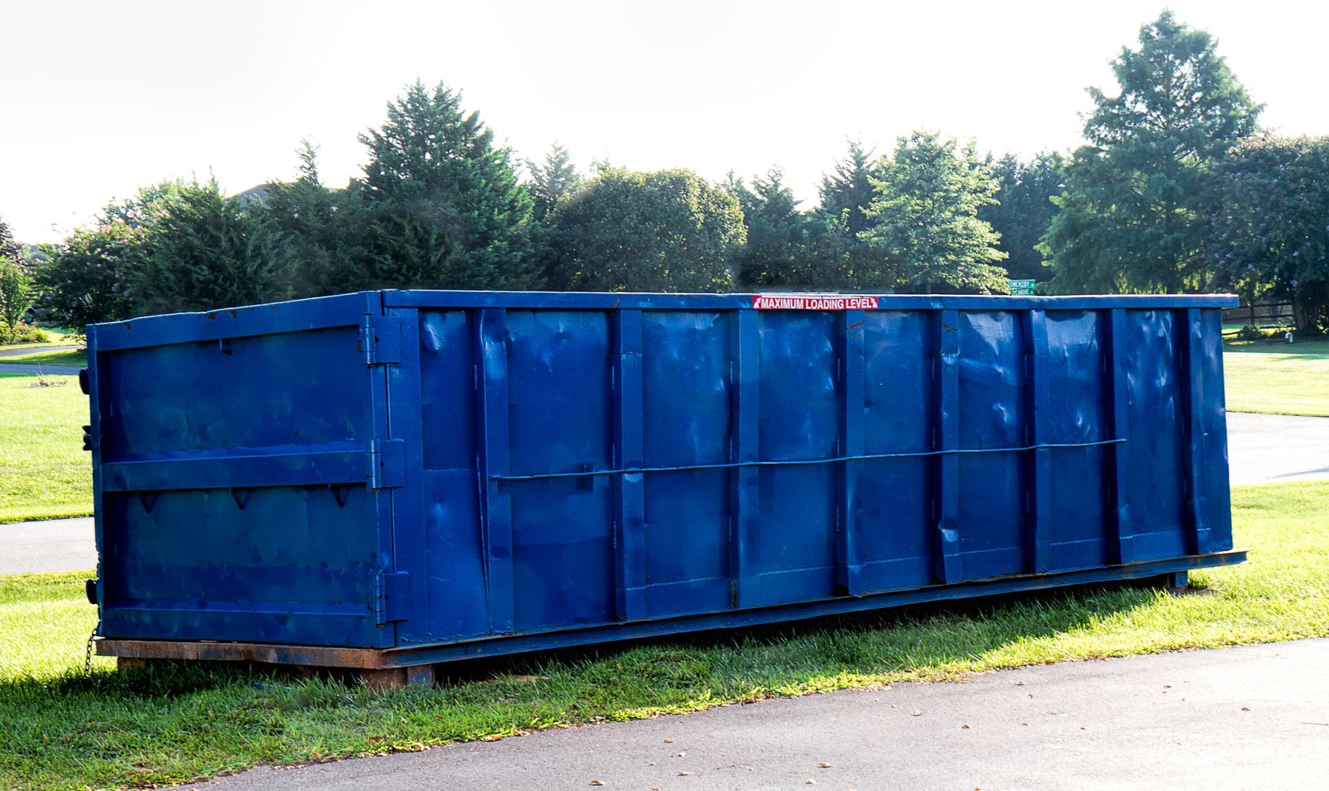 A large blue dumpster is sitting on the side of a road.