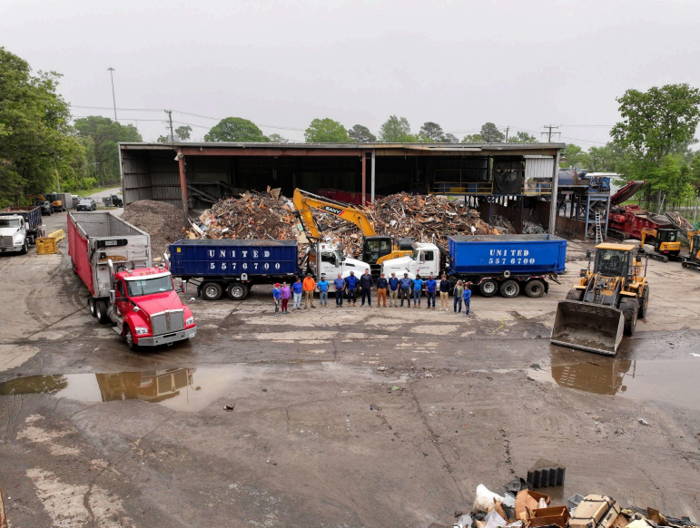 A group of trucks are parked in front of a large pile of trash.