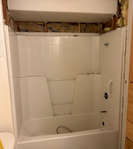 A man is standing on a ladder in a kitchen painting the ceiling.