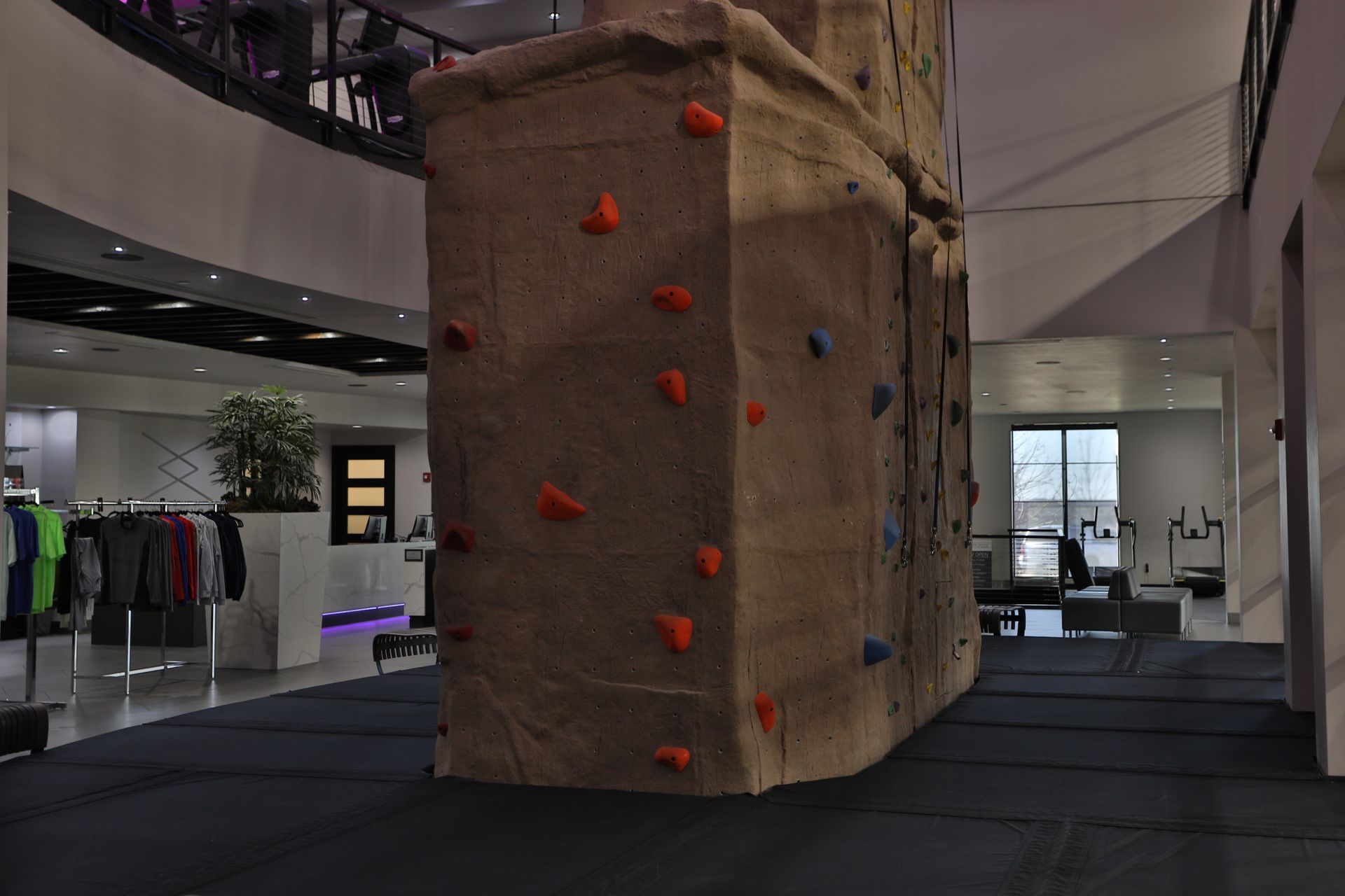 Indoor climbing wall with colorful holds. Retail area in the background.