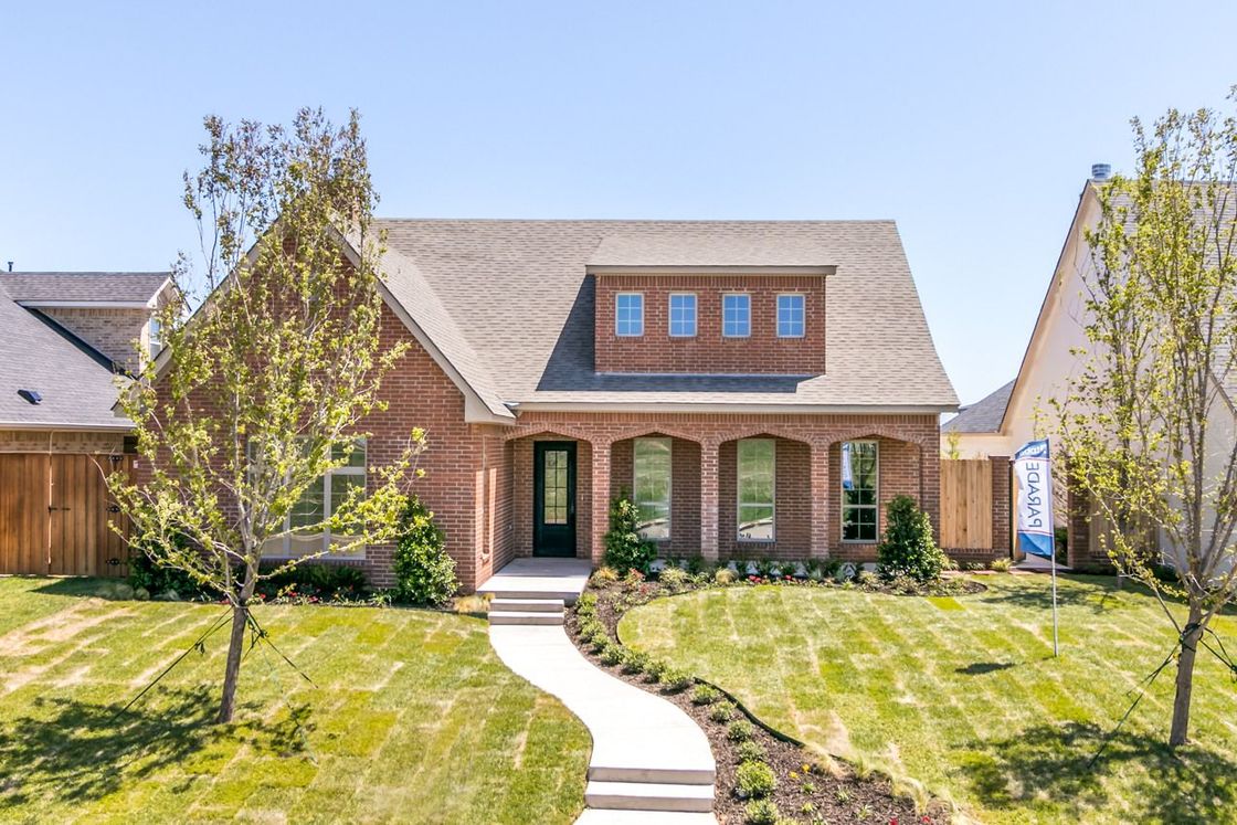 Red brick house with manicured lawn, blue sky, and a winding walkway.