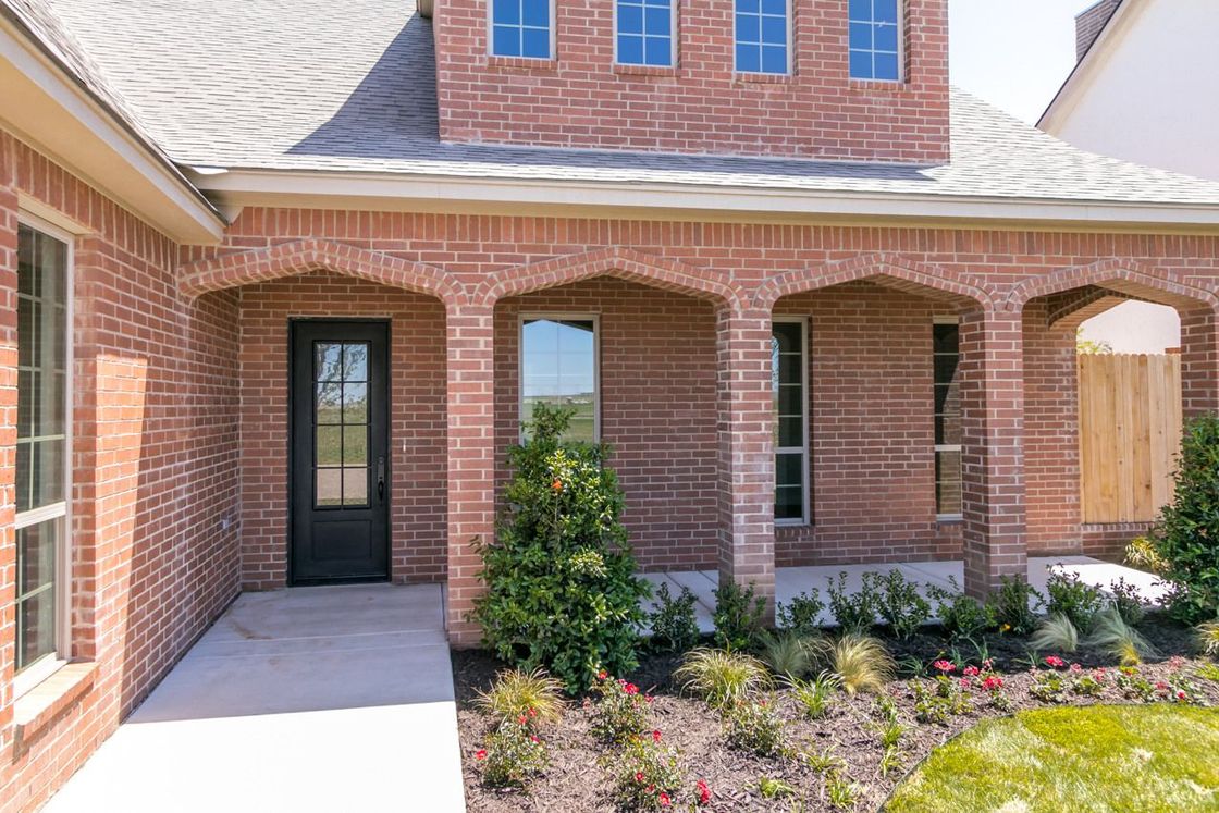 Red brick house exterior with arched porch, black door, and landscaped yard.