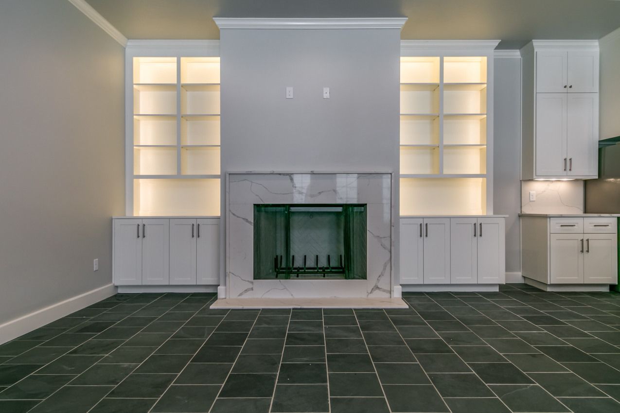 Living room with fireplace, built-in shelves, white cabinets, marble, and gray walls. Dark stone floor.