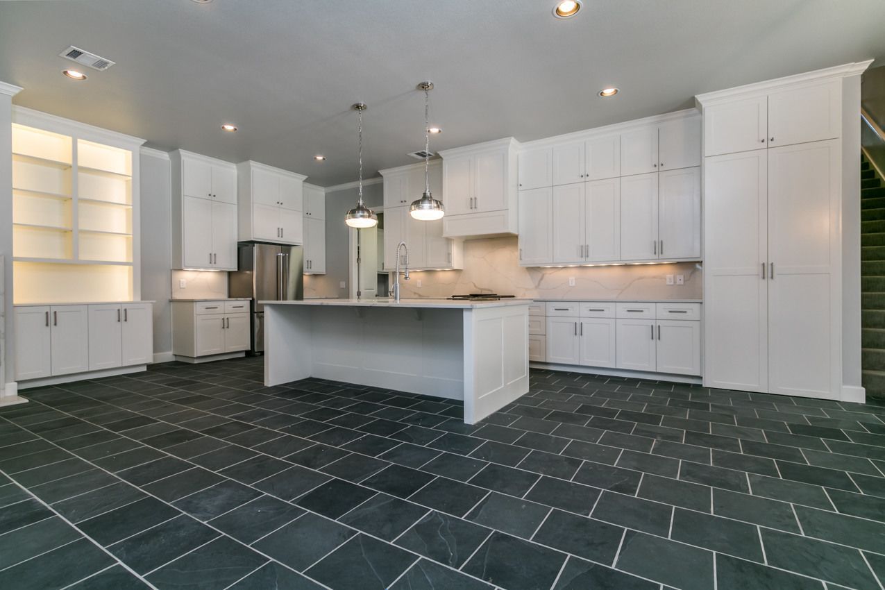 Modern white kitchen with stainless steel appliances and dark gray tiled floor.