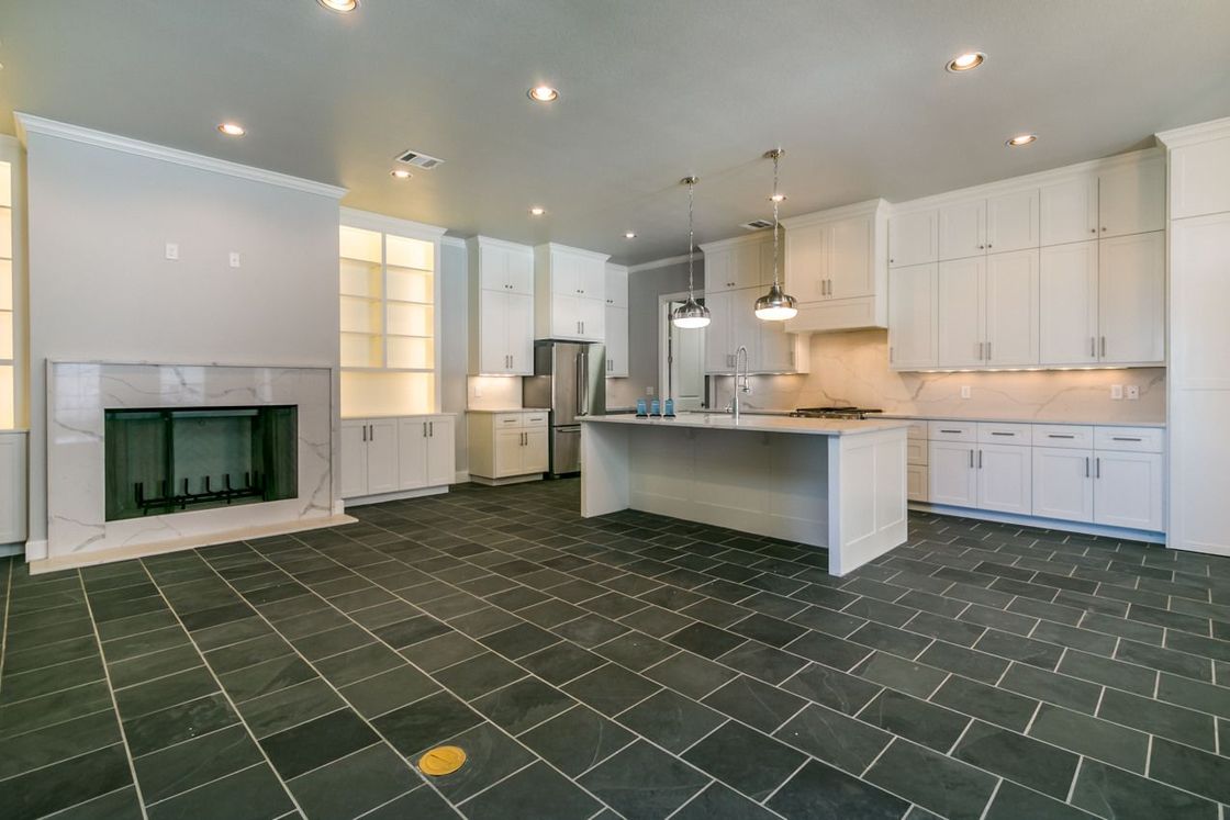 Spacious, modern kitchen with white cabinetry, island, fireplace, stainless steel appliances, and dark tile floor.