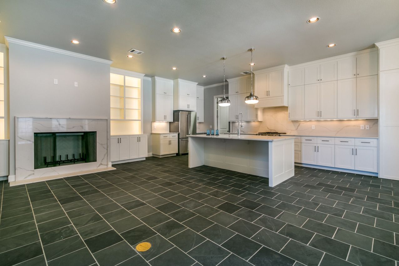 Spacious, modern kitchen with white cabinetry, island, fireplace, stainless steel appliances, and dark tile floor.