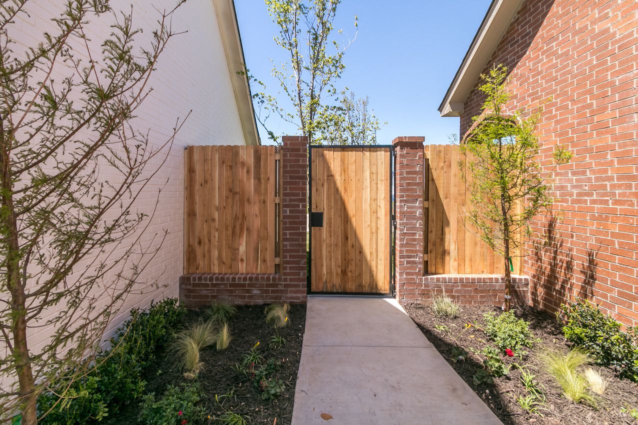 Wooden gate and fence framed by brick columns and walls. Concrete path and landscaping in front.