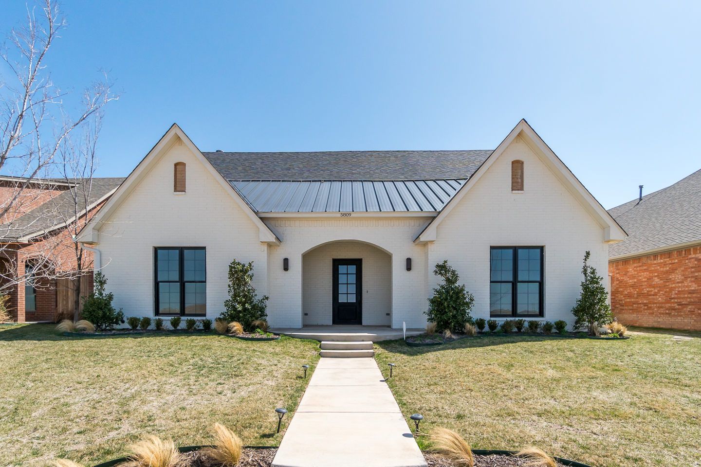 White house with black windows and door, gray roof, and a concrete path.
