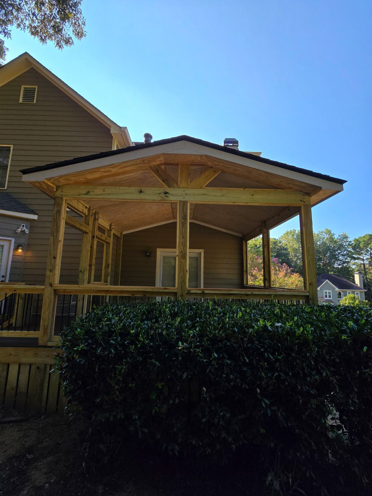 Wooden screened porch addition to a house, against a blue sky, framing a view.