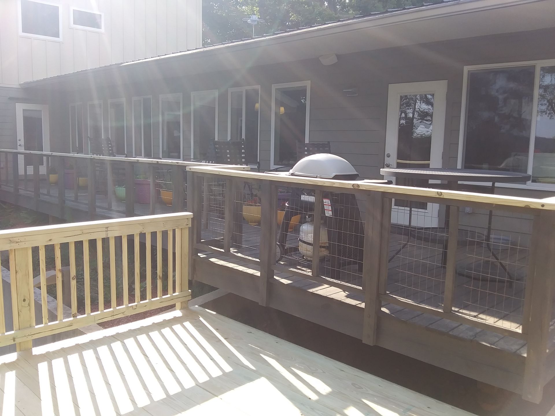 Wooden deck with railings, connected to a building with multiple doors and windows. Sunny outdoor setting.