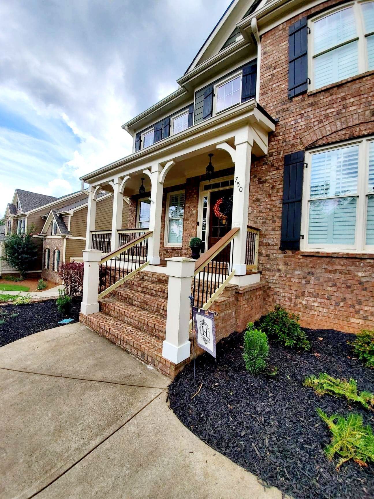 Brick house with a porch, steps, and black mulch landscaping under a cloudy sky.