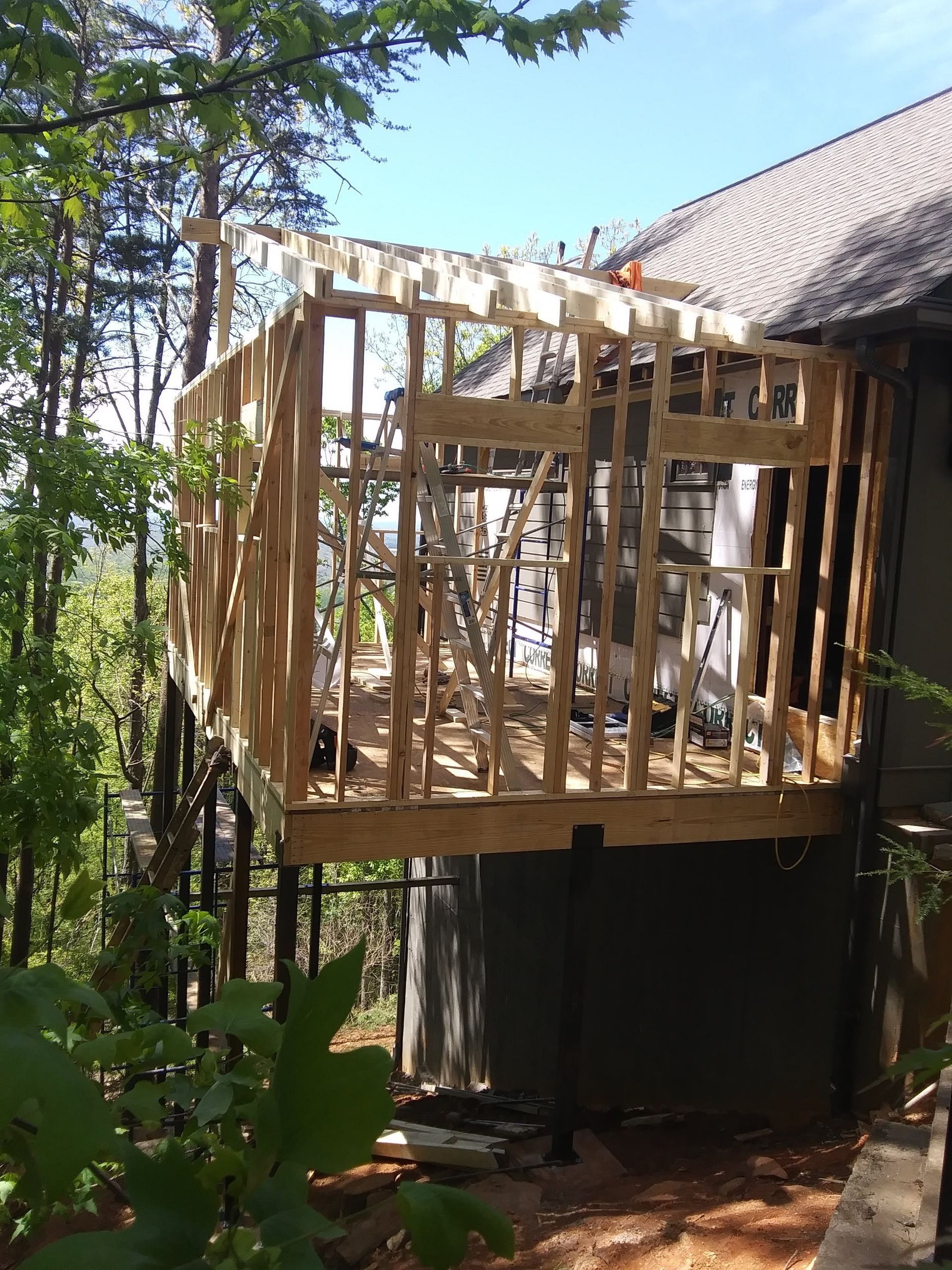 Wooden deck framing attached to a house; construction in progress, sunny outdoors.