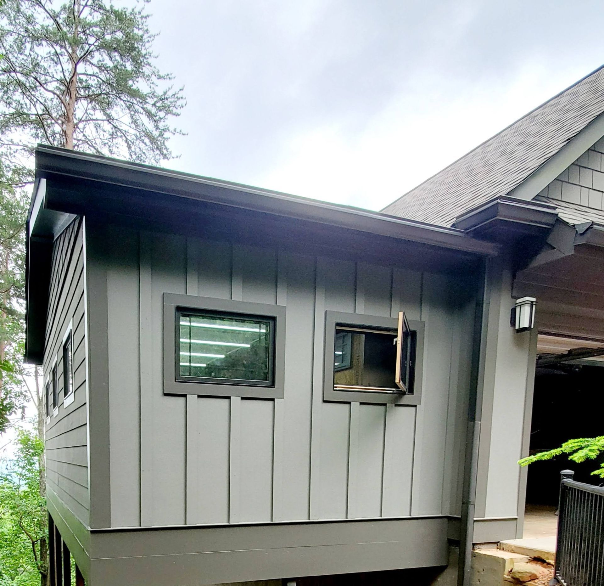 Gray cabin exterior with two windows, one open. Overcast sky.