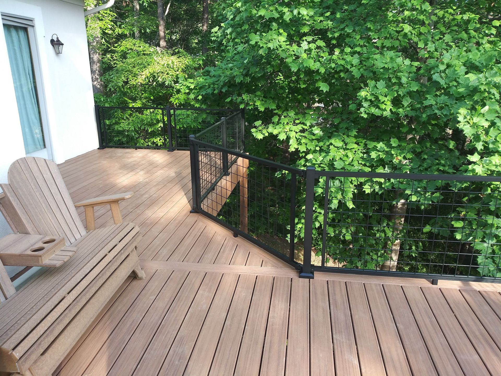 Wooden deck with black metal railing overlooking trees. Adirondack chairs are on the deck.