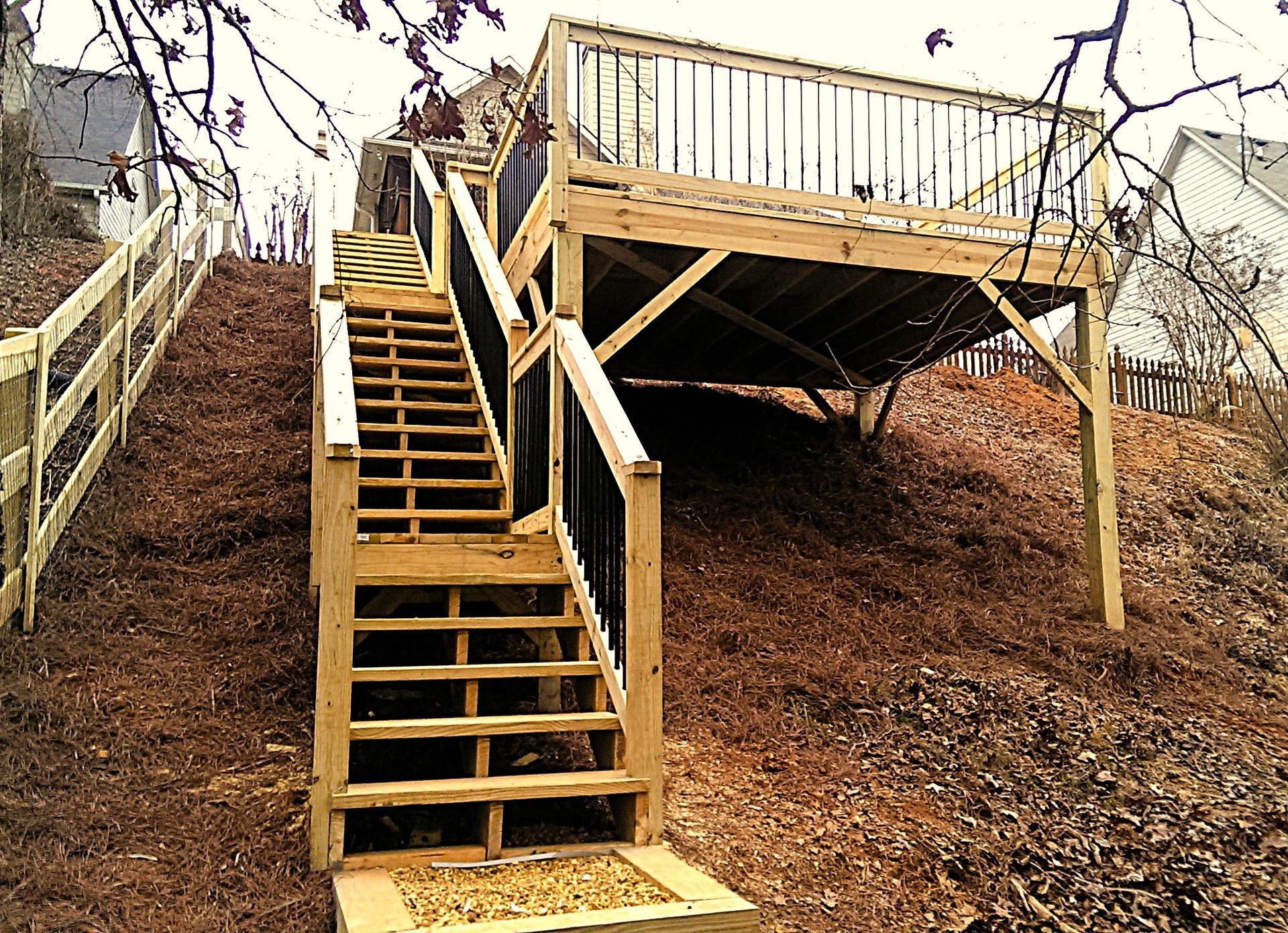 Wooden deck and stairs on a hillside. The deck has a railing, and the stairs lead to a lower landing.