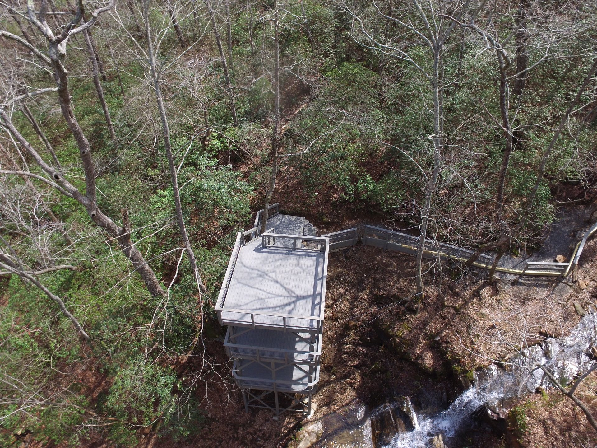Overhead view of a wooden observation platform in a forest next to a flowing stream.