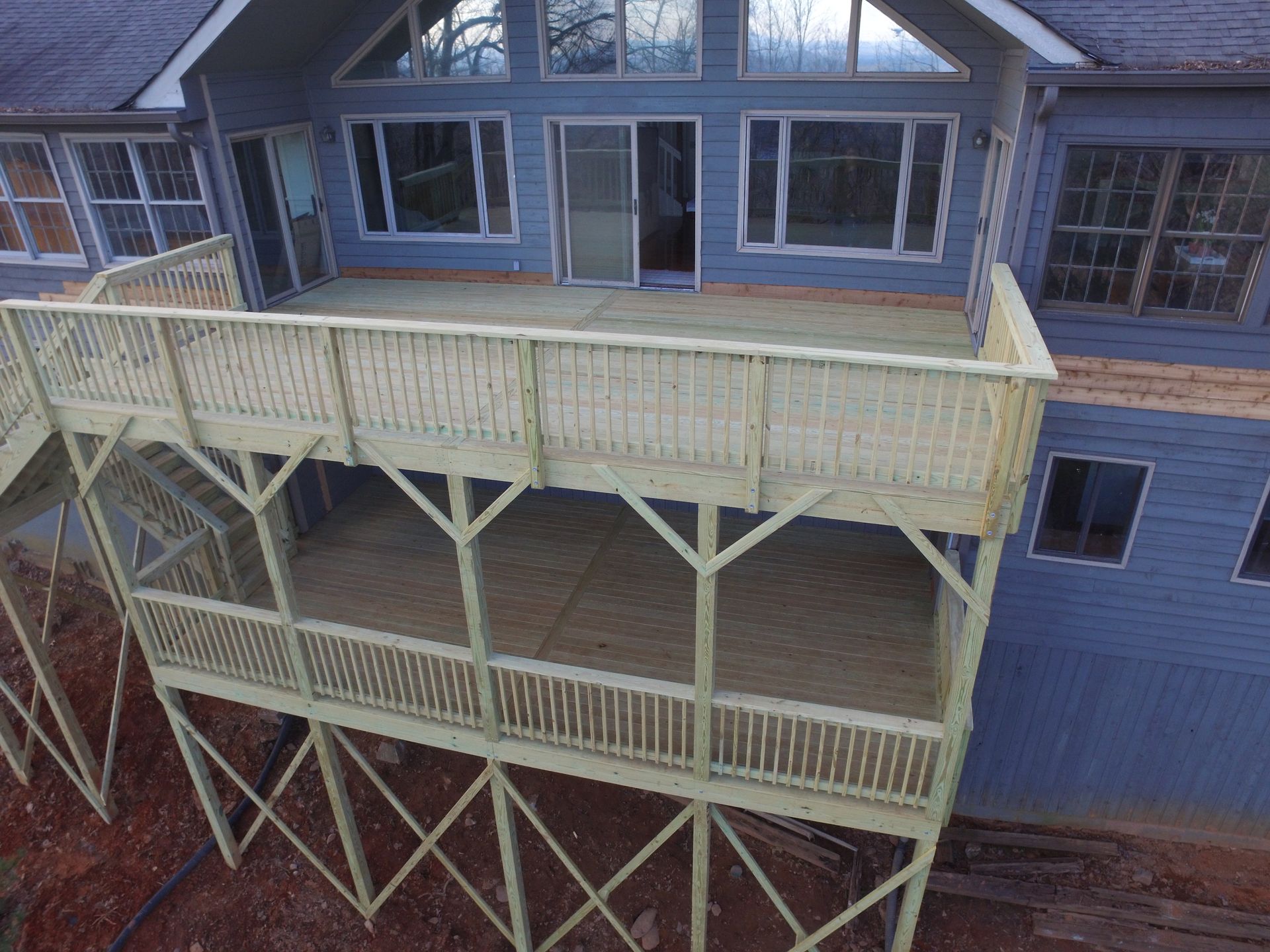 Elevated wooden deck attached to a blue house, supported by wooden beams, overlooking a yard.