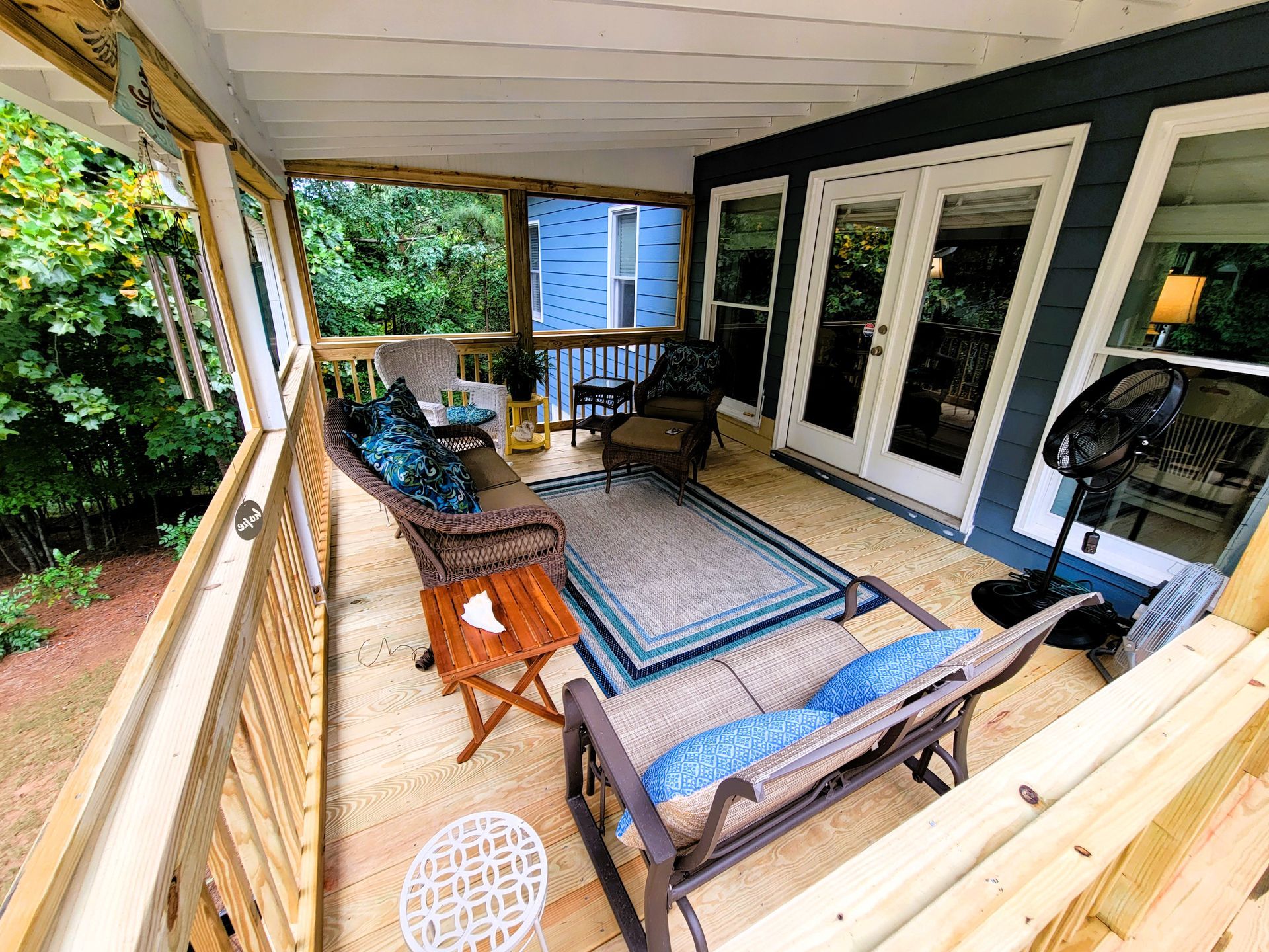 Screened porch with seating, rug, and French doors leading inside. Wooden deck.