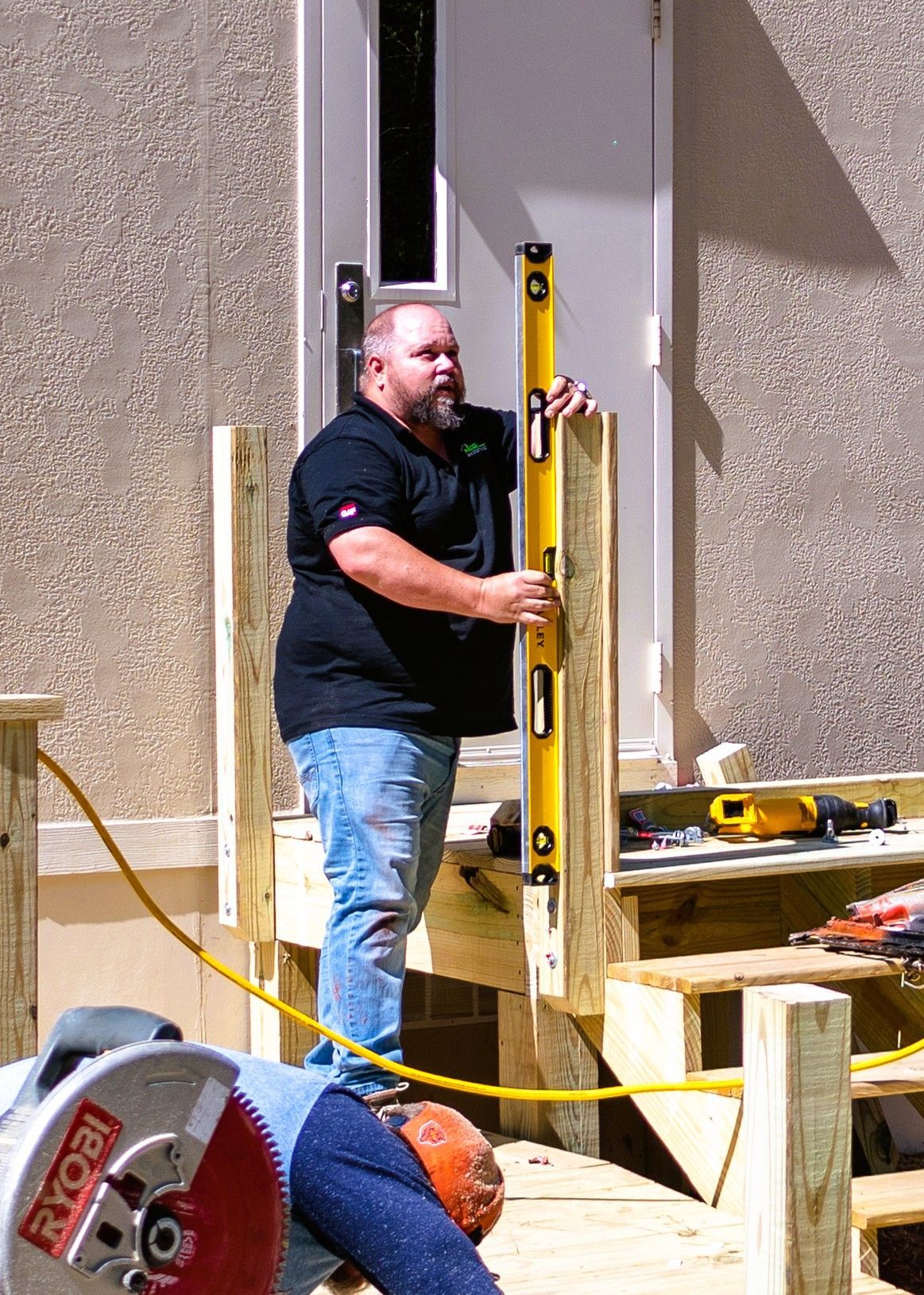 Man using a level to install a wooden post on a deck, sunny day.