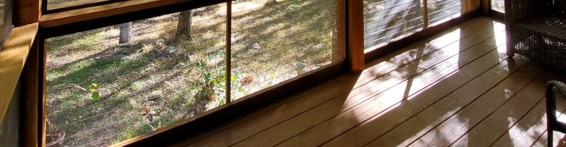 View from a wooden deck through a window, looking out to grass and trees.