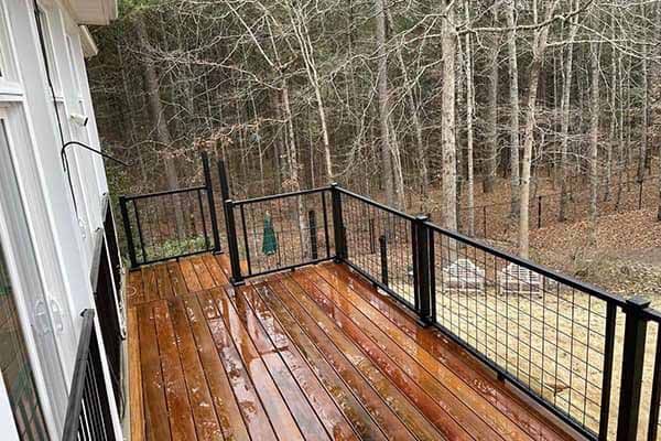 Wooden deck with black metal railing overlooking a wooded area. Wet wood planks.