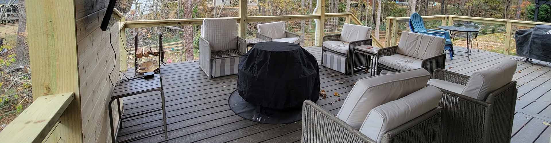Outdoor deck with seating, covered grill, and wooden railing overlooking trees.