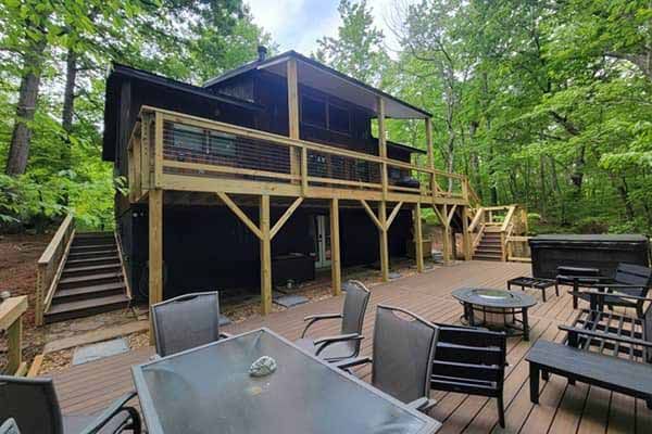Cabin with new wooden deck and stairs, surrounded by trees. Outdoor furniture on patio.
